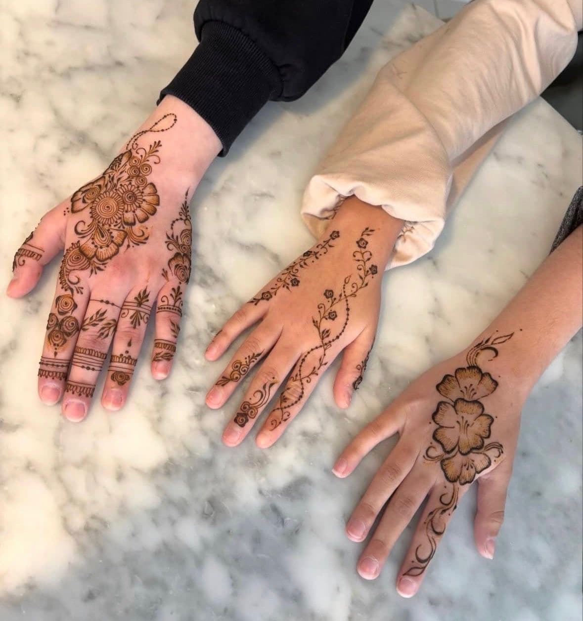 Three hands resting on marble, each with a different brown henna design