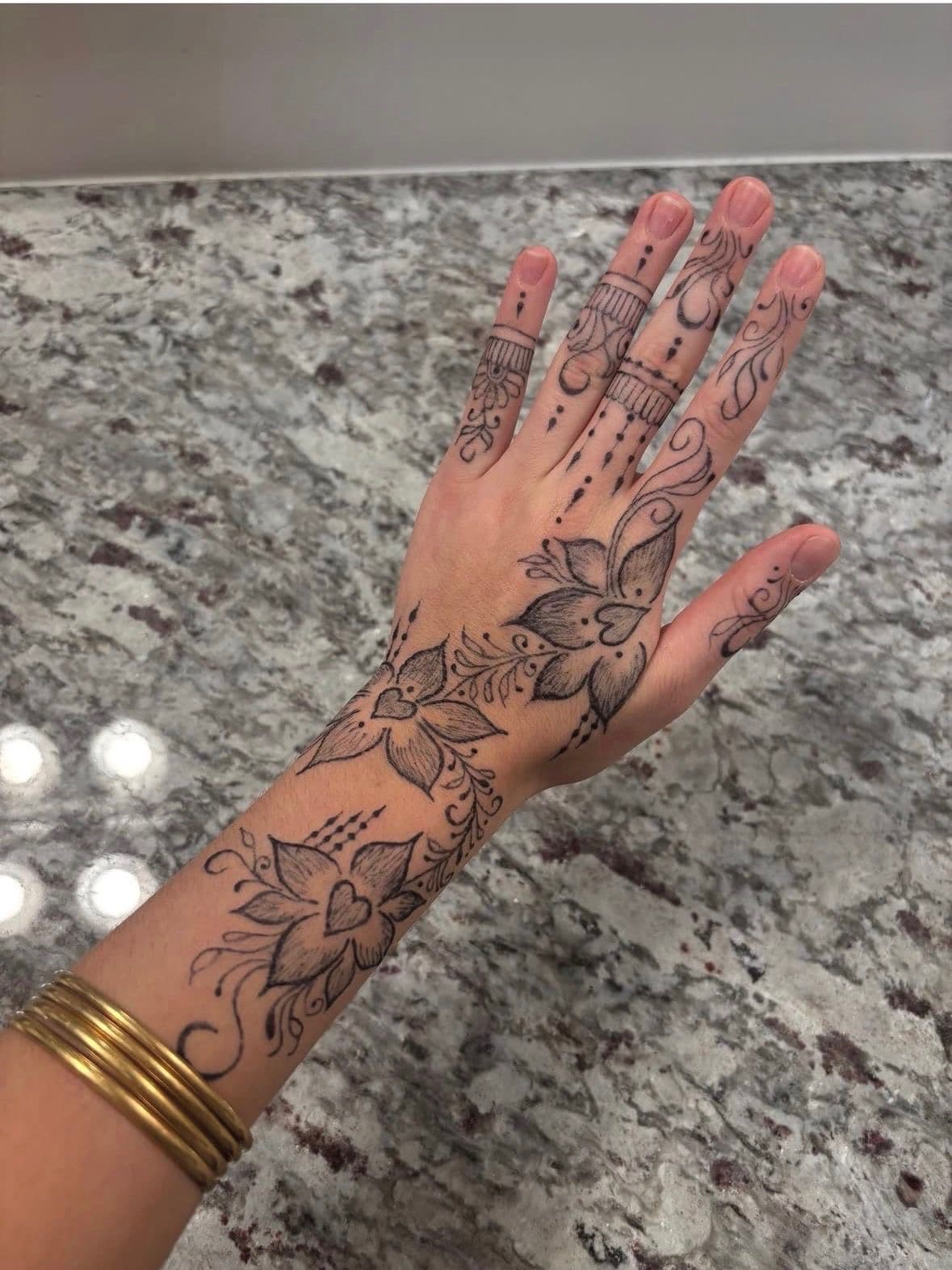 Fine line jagua florals down the back of the hand and forearm against marble